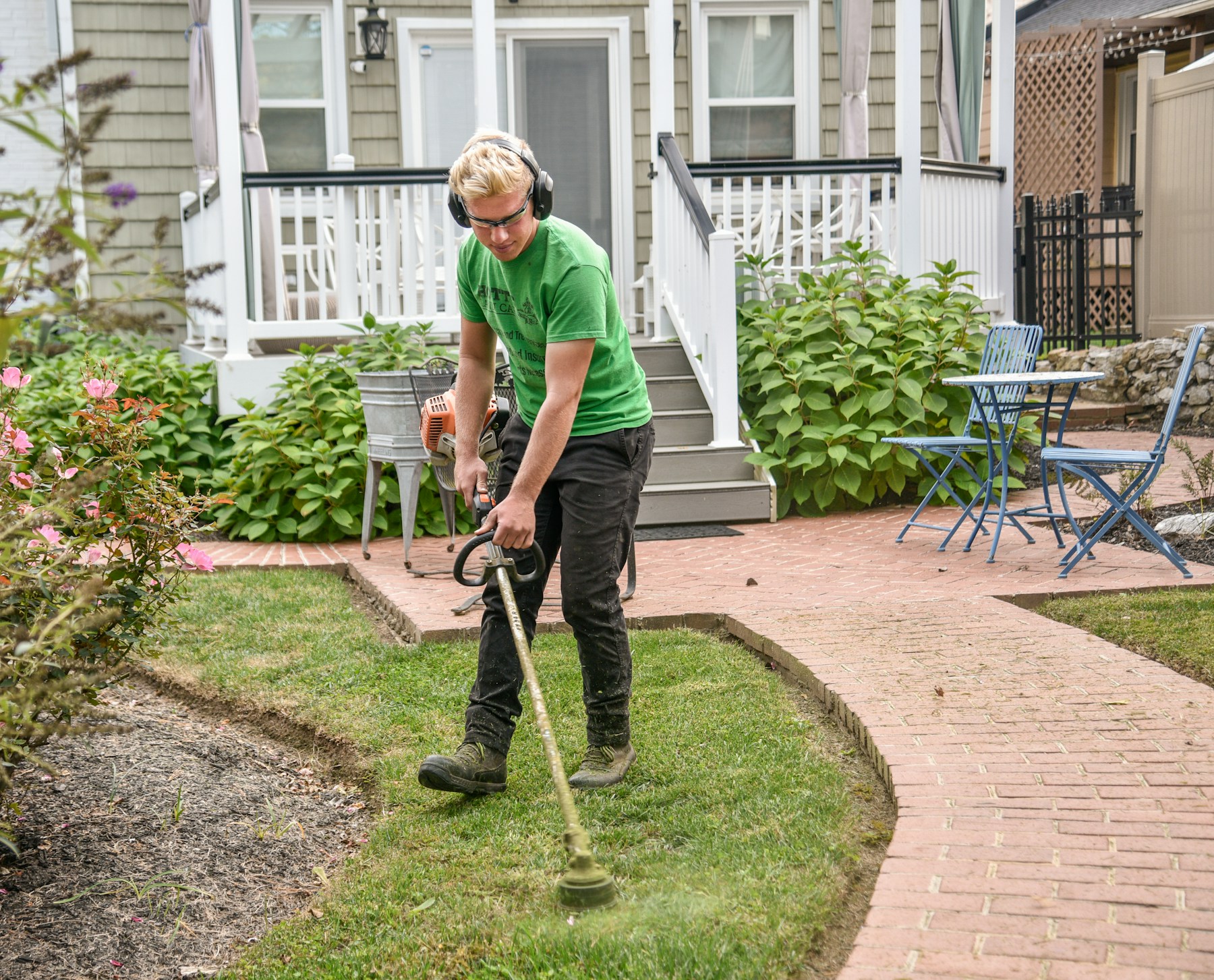 A lawn care professional trimming beside a garden